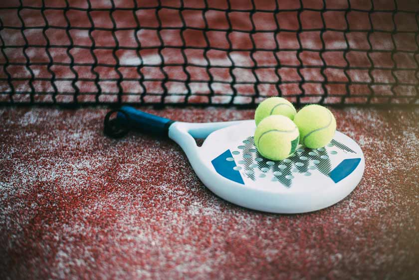 Padel Tennis Schläger und Bälle liegen vor dem Netz auf rotem Boden